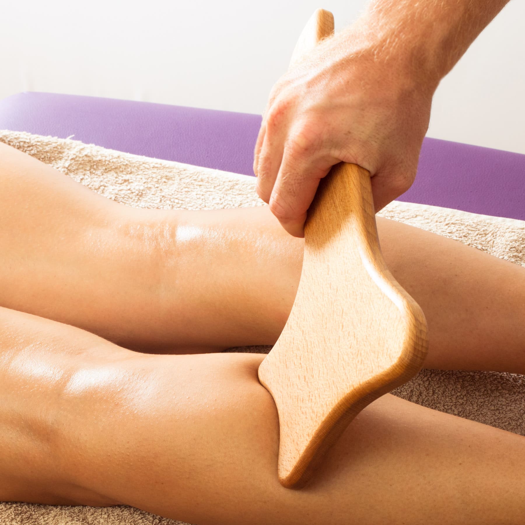 Person using a wooden brush on their leg with a white background